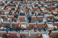 Top down view of conference attendees in auditorium seats taking notes