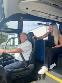 John sitting in the drivers seat of a bus with Elyce sititng behind him