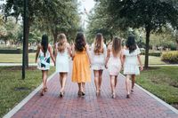 The back of a group of girls dressed up nicely and holding hands walking away from the camera.